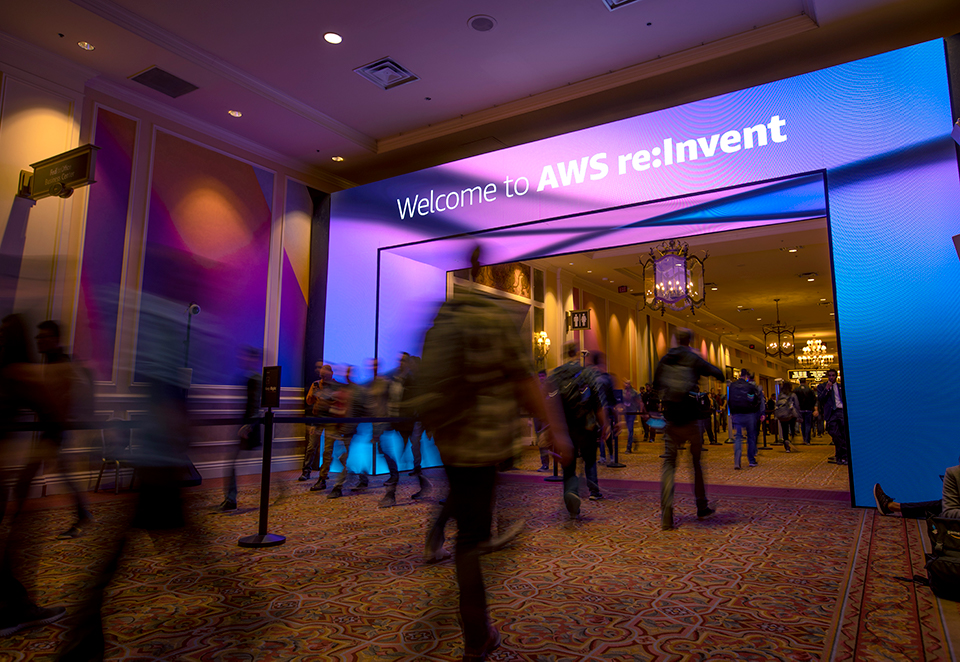 A motion-blurred picture of people walking under a Welcome to AWS re:Invent sign